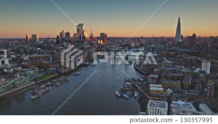 Tower Bridge and The Shard are reflecting on River Thames at sunset, creating a stunning cityscape view of London's business district. Evening city skyline under vibrant sky. Drone flight Tower Bridge and The Shard are reflecting on River Thames at sunset, creating a stunning cityscape view of London's business district. Evening city skyline under vibrant sky. Drone flight 130357995