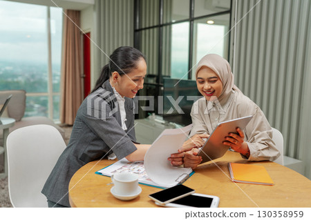 Two businesswomen are collaborating in a modern office to share ideas and ambitions 130358959
