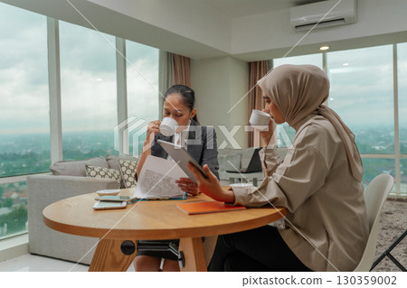 Professional Women Engaging in Discussion Over Coffee in Modern Office Setting Professional Women Engaging in Discussion Over Coffee in Modern Office Setting 130359002