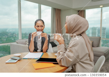 Two women are enjoying coffee together in a modern office workspace setting today Two women are enjoying coffee together in a modern office workspace setting today 130359054