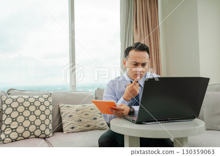 A Business Professional Engaged in Remote Work Utilizing a Laptop and Taking Notes A Business Professional Engaged in Remote Work Utilizing a Laptop and Taking Notes 130359063