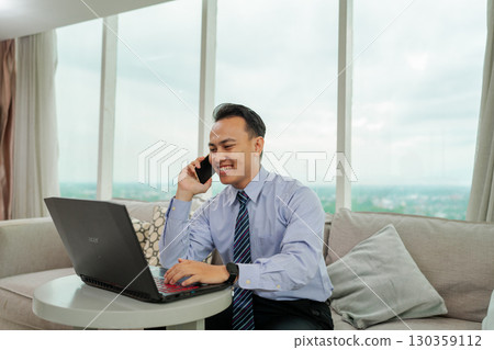 Professional Man Working on Laptop While Talking on Phone in Modern Office Professional Man Working on Laptop While Talking on Phone in Modern Office 130359112