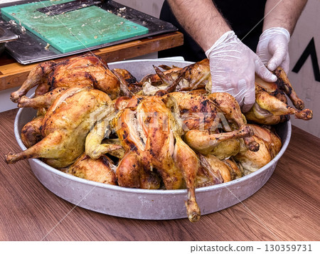Cook slicing roasted chicken on a cutting board in a kitchen setting. Culinary preparation, food service, and gastronomy. Cook slicing roasted chicken on a cutting board in a kitchen setting. Culinary preparation, food service, and gastronomy. 130359731