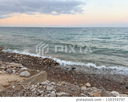 The sea reflects soft evening light under cloudy sky with distant horizon line. Calm waves, marine ecology and coastal landscape in seasonal outdoor environment. 130359797