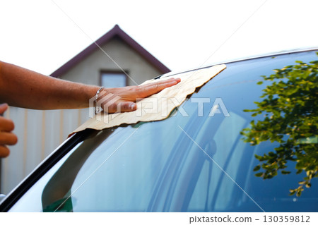a hand with a rag, cleaning a car windshield. car window cleaning close-up. hand wiping windshield rag. professional car wash detailing a hand with a rag, cleaning a car windshield. car window cleaning close-up. hand wiping windshield rag. professional car wash detailing 130359812