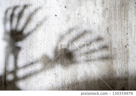 Abstract image of a skeleton hand shadow cast onto a grungy and aged cement surface. The texture features cracks and a shadow overlay. Concept of Spooky Halloween 130359979
