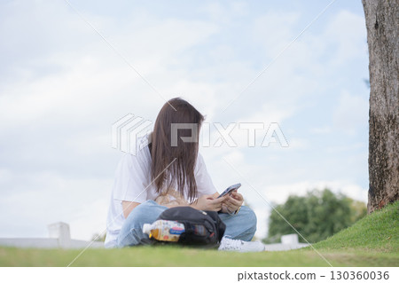 Relax and wellness concept with woman sit and use phone in garden and mountain background at chiangmai thailand in raining season 130360036