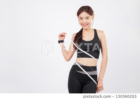 Holding the tape with both hands and adjusting the tape carefully, the slim woman looks happy and healthy, confident in her fit and sporty body. isolated studio white background 130360283