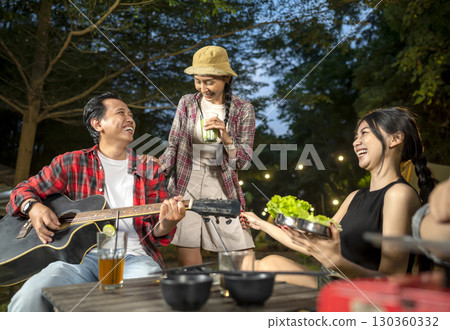 Indonesian southeast asian people cooking sliced marinated beef bulgogi on a grill pan. One of them is holding an acoustic guitar. Scene of the lifestyle of enjoying food in a natural setting 130360332