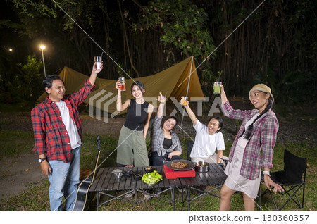 Indonesian southeast asian people relaxing together outdoors and enjoying refreshing drinks while cooking sliced beef on a grill pan. The scene of the lifestyle of enjoying food in a natural setting Indonesian southeast asian people relaxing together outdoors and enjoying refreshing drinks while cooking sliced beef on a grill pan. The scene of the lifestyle of enjoying food in a natural setting 130360357