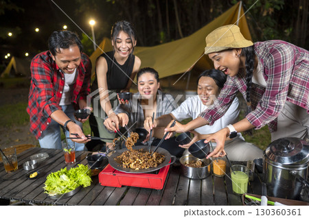 Indonesian southeast asian people with chopsticks cooking sliced marinated beef bulgogi on a round grill pan with onions. The scene of the lifestyle of enjoying food in a natural setting Indonesian southeast asian people with chopsticks cooking sliced marinated beef bulgogi on a round grill pan with onions. The scene of the lifestyle of enjoying food in a natural setting 130360361