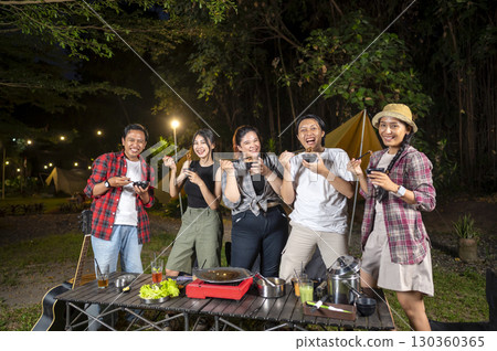Indonesian southeast asian people are enjoying a meal, using chopsticks to serve themselves a barbecue meal from small black bowls. The scene of the lifestyle of enjoying food in a natural setting 130360365