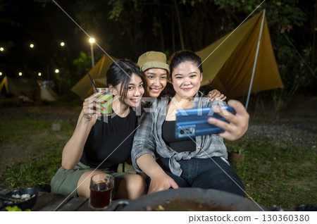 Indonesian southeast asian women capturing a selfie using a cellphone together outdoors and enjoying refreshing drinks. The scene of the lifestyle of enjoying food in a natural setting 130360380