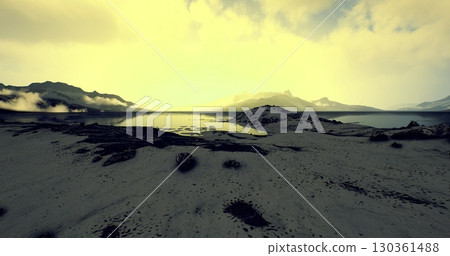 A tranquil landscape showcases a calm body of water reflecting sunlight. Distant mountains create a stunning backdrop, with clouds gently floating above the horizon during early morning. 130361488