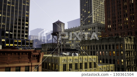 A historic water tower is prominently placed atop a yellow building, surrounded by skyscrapers under a dusky sky, showcasing the blend of architecture and urban life after sunset. 130361504