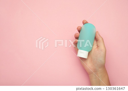 Hand holding blank blue plastic tube on pink background. Cosmetic beauty product branding mockup. Hand holding blank blue plastic tube on pink background. Cosmetic beauty product branding mockup. 130361647