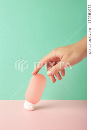 Hand holding blank pink plastic tube on mint background. Cosmetic beauty product branding mockup. Vertical photo 130361651