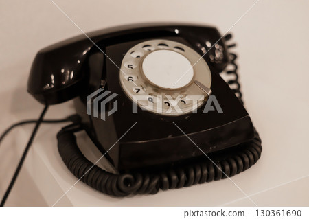 A vintage rotary telephone rests on a clean, minimalist table against a neutral backdrop. The device highlights the charm of old-school communication methods in a contemporary setting 130361690