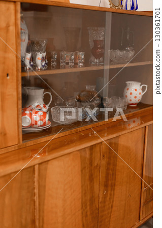 A collection of vintage glassware and ceramic items is displayed in a wooden cabinet. The warm light of the day highlights the craftsmanship of the pieces, creating an inviting atmosphere 130361701