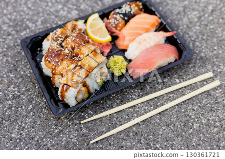 A variety of sushi including eel and salmon with garnishes of lemon and wasabi placed on a textured surface with chopsticks nearby for easy eating A variety of sushi including eel and salmon with garnishes of lemon and wasabi placed on a textured surface with chopsticks nearby for easy eating 130361721
