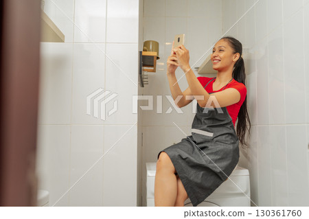 A Woman Taking a Fun Selfie While Sitting on the Toilet Using Her Smartphone A Woman Taking a Fun Selfie While Sitting on the Toilet Using Her Smartphone 130361760