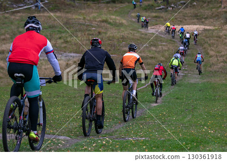 Group cyclists riding uphill trail behind each other at mountain bike race 130361918