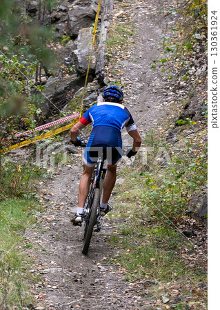 Rear view cyclist riding uphill on forest trail at mountain bike competition Rear view cyclist riding uphill on forest trail at mountain bike competition 130361924