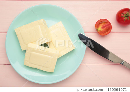 Processed cheese in foil and tomato on mint plate on pink background 130361971