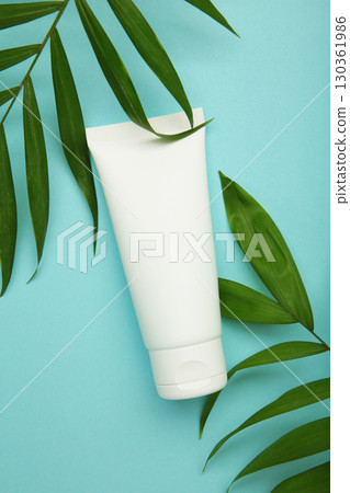 White cosmetic tube with green leaves on blue background. 130361986