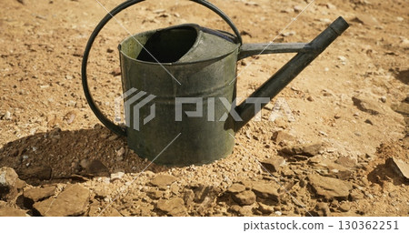A weathered metal watering can lies on cracked, dry earth bathed in warm sunlight. The scene reflects the challenges of gardening in a dry environment, emphasizing resilience. A weathered metal watering can lies on cracked, dry earth bathed in warm sunlight. The scene reflects the challenges of gardening in a dry environment, emphasizing resilience. 130362251