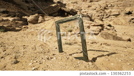 A rectangular frame positioned upright in a sandy terrain showcases unique rock formations in the background, highlighting the contrast between nature and man made objects during daylight. 130362253