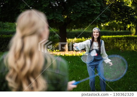 Friends enjoy a lively game of badminton in a sunlit park Friends enjoy a lively game of badminton in a sunlit park 130362320
