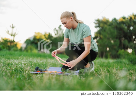 Woman prepares for outdoor workout in sunlit green field surrounded by trees Woman prepares for outdoor workout in sunlit green field surrounded by trees 130362340