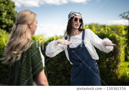 Fashionable friends enjoying a sunny day outdoors while chatting playfully Fashionable friends enjoying a sunny day outdoors while chatting playfully 130362356