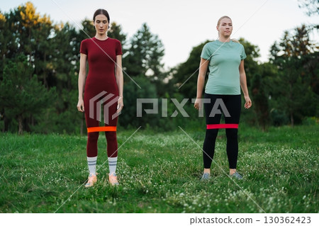 Two women practicing fitness outdoors with resistance bands in a park Two women practicing fitness outdoors with resistance bands in a park 130362423