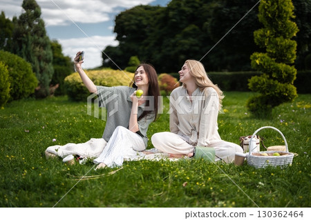 Friends enjoying a sunny picnic while capturing joyful moments together 130362464