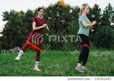 Women engaging in outdoor fitness routine with resistance bands in nature Women engaging in outdoor fitness routine with resistance bands in nature 130362485