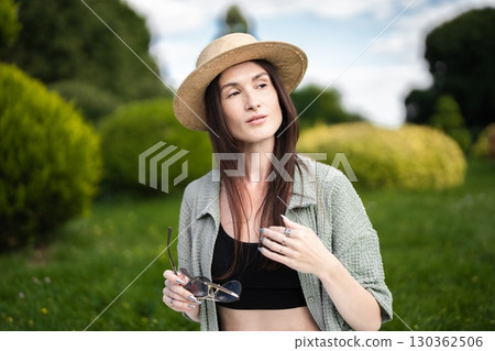 Woman enjoying a sunny day in a green park wearing a stylish hat 130362506