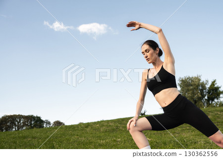 Elegant warrior pose in a sunny green park during afternoon practice Elegant warrior pose in a sunny green park during afternoon practice 130362556