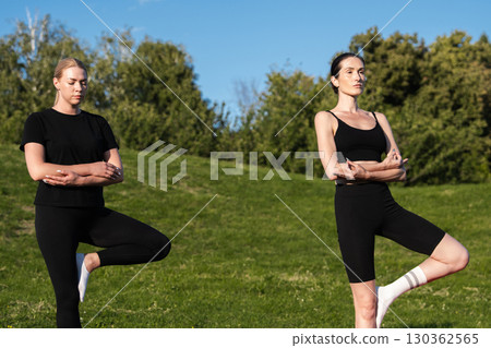 Two women practicing yoga in a sunny park during a tranquil afternoon 130362565