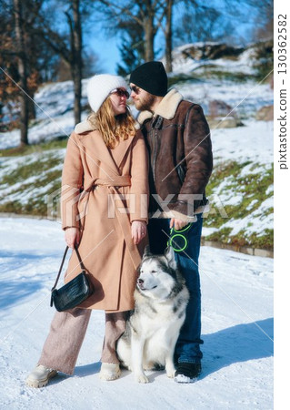 Couple enjoying winter stroll with their dog on a snowy day in the park 130362582