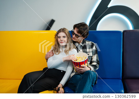 Couple enjoying popcorn while relaxing in a colorful cinema seating area Couple enjoying popcorn while relaxing in a colorful cinema seating area 130362599
