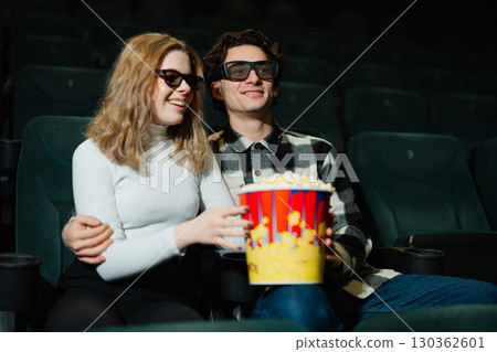 Couple enjoying a movie together in a theater with popcorn Couple enjoying a movie together in a theater with popcorn 130362601
