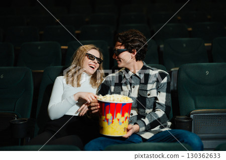 Couple enjoys a movie date while sharing popcorn in a theater Couple enjoys a movie date while sharing popcorn in a theater 130362633