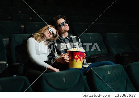 Couple enjoys movie together in theater with popcorn in hand Couple enjoys movie together in theater with popcorn in hand 130362638