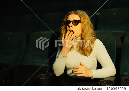 Woman enjoying a suspenseful movie in a theater during evening show 130362639