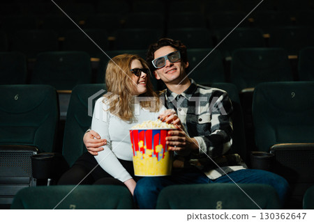 Young couple enjoying a movie date night with popcorn in a theater Young couple enjoying a movie date night with popcorn in a theater 130362647