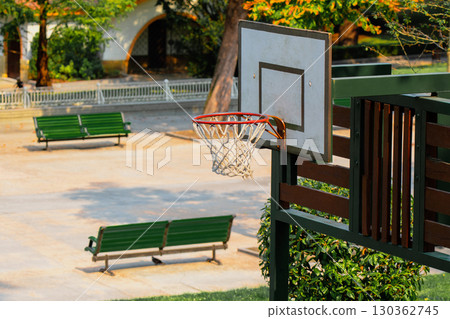 Natural park walking area with basketball hoop and green benches in summertime 130362745
