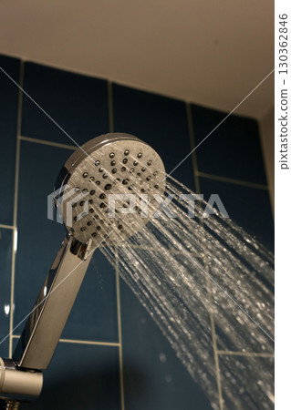 A chrome handheld shower head spraying water A chrome handheld shower head spraying water 130362846