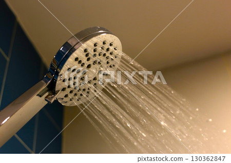 A chrome handheld shower head spraying water A chrome handheld shower head spraying water 130362847